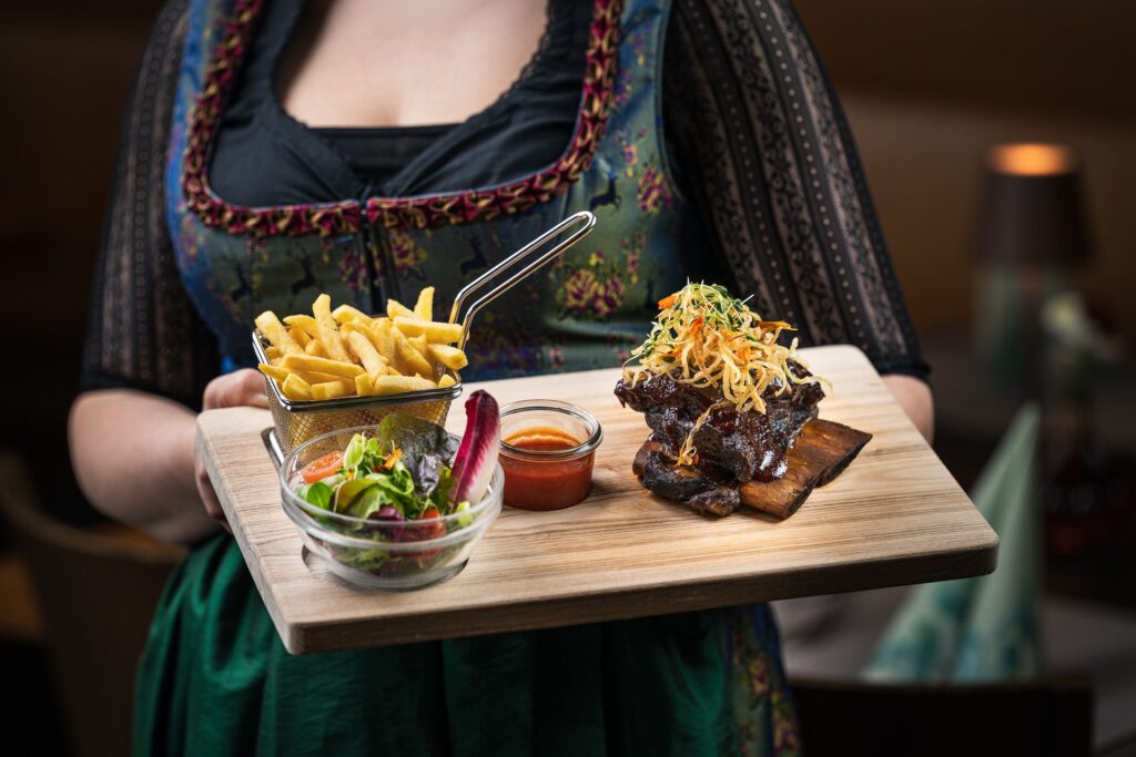 Service im Dirndl serviert Spareribs mit Pommes und Salat